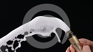 Female hand uncorking bottle of champagne on black background. Explosion of sparkling white wine with foam and bubbles