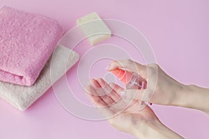 Female hand using antibacterial hand sanitizer on light pink background