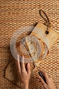 Female hand using long knife cutting bread on wood block showing air flour texture.