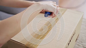 Female hand using sharp cutter knife slashing tape on cardboard box to open carton parcel.