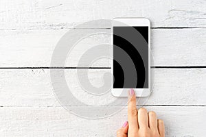 Female hand using smartphone with empty screen on rustic wooden background.