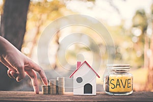 Female hand walking on coins with save word and model house on table in nature bokeh background