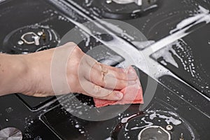 Female hand washes gas stove, glass ceramic surface. Red sponge and white foam