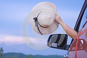 Female hand waving her wide brim hat while sticking out of red car window on country road