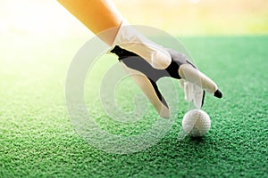 Female hand wearing white professional gloves with the left hand putting golfball on the rubber tee grass course