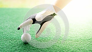 Female hand wearing white professional gloves with the left hand putting golfball on the rubber tee grass course