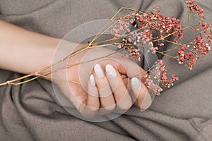 Female hand with white nail design. Female hand holding pink autumn flower. Woman hand on beige fabrick background