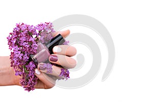 Female hand with white and purple nail design holding lilac flowers
