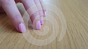 Female hand with white skin and pink short nails scratching a wooden table