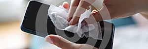 Female hand wipes smartphone with disinfectant napkin from bacteria photo