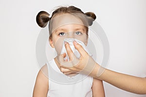 Female hand wiping nose of little kid girl. Small girl in white top blows her nose in white wet rag on white background