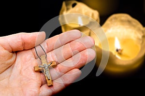 Female hand with wooden cross on candles background