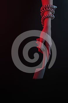 Female hand wrapped in a cable holds a telephone receiver on a black background with a neon red light
