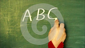 Female hand writing `ABC` on a chalkboard and drawing a smiley under the letters