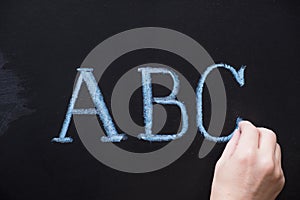 Female hand writing alphabet on black chalkboard. Educational background with ABC letters with copy space