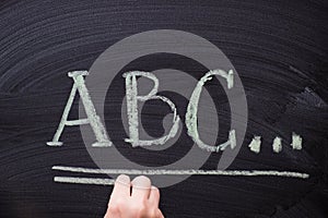 Female hand writing alphabet on black chalkboard. Educational background with ABC letters with copy space