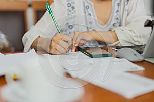 Female hand writing on financial papers while paying bills online using laptop.