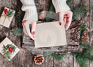 Female hand writing a letter to Santa on wooden background with Christmas gifts, bark texture, Fir branches