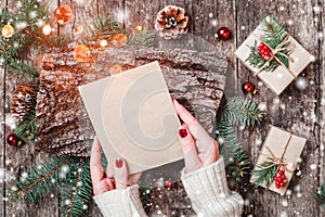 Female hand writing a letter to Santa on wooden background with Christmas gifts, bark texture, Fir branches