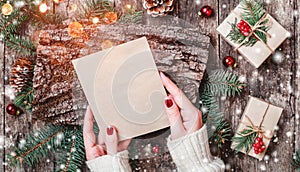 Female hand writing a letter to Santa on wooden background with Christmas gifts, bark texture, Fir branches, pine cones, red decor