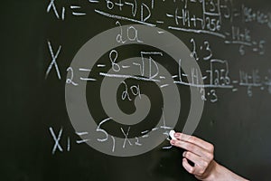 female hand writing math formulas on the classboard