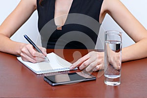 Female hand writing with a pen on the table next to the smartphone