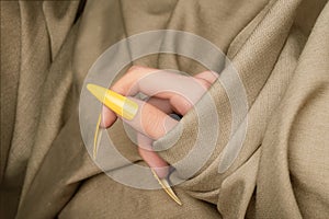 Female hand with yellow nail design. Long nail polish manicure. Woman hand on beige fabric background