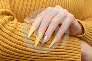 Female hand with yellow nail design. Long nail polish manicure. Woman manicure with gitter gold long nail art photo