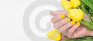 Female hand with yellow nail design. Yellow nail polish manicure. Female hand with yellow tulips on white background