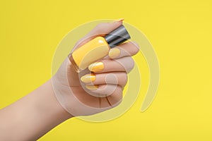 Female hand with yellow nail design. Yellow nail polish manicure. Woman hold yellow varnish on yellow background