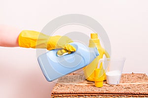 a female hand in a yellow rubber glove holds a measuring cap with washing gel