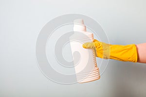 a female hand in a yellow rubber glove holds a white bottle of bleach for clothes