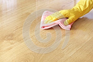 A female hand in a yellow rubber glove washes a wooden parquet floor with a pink microfiber cloth.