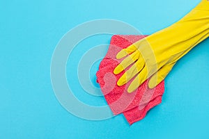 A female hand in a yellow rubber protective glove with a micro fiber red rag wiping a blue wall from dust. A maid or housewife