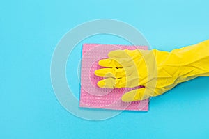 A female hand in a yellow rubber protective glove with a micro fiber red rag wiping a blue wall from dust. A maid or housewife