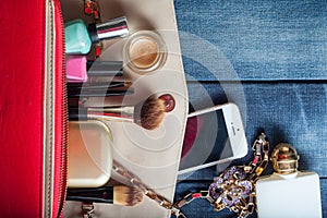 Female handbag with cosmetics and mobile on jeans background