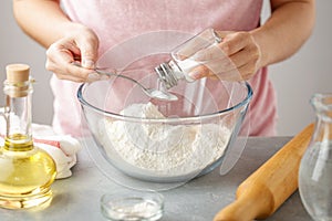 Female hands add salt into glass bowl with flour.