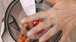 Female hands add spicy red chili pepper into blender to cook vegetable sauce. Top view, vegan and vegeterian food