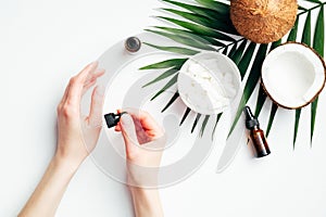 Female hands applying coconut oil for hand skin moisturizing. Flat lay composition with woman`s hands, tropical palm leaf,