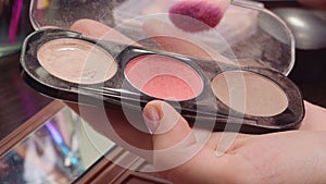 Female hands applying make-up blush from face cosmetic palette close up