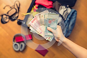 Female hands with Asian money and foreign passport. Suitcase with things on the floor. Travel concept