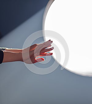 Female hands on the background of a round window in the rays of sunlight