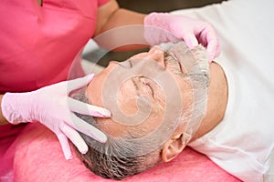 Female hands of beautician examining face of man in chair