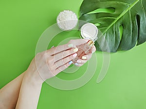 Female hands beautiful manicure treatment creative Monstera leaf, cosmetic cream on a color background