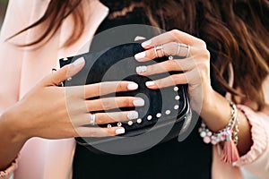 Female hands with beautiful nail polish and rings holding small black bag.
