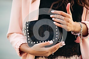 Female hands with beautiful nail polish and rings holding small black bag.