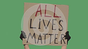 Female hands in black gloves hold a poster from a cardboard box with the words ALL LIVES MATTER. Protest against racism