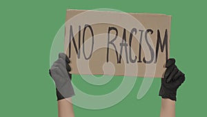 Female hands in black gloves pick up a poster from a cardboard box that reads NO RACISM. The concept of the global