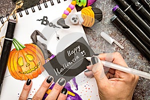 Female hands with black nails drawing halloween illustration with markers on wooden table top view