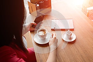 Female hands with a black phone, close-up, background of a cup of coffee, table, notebook. Business lunch